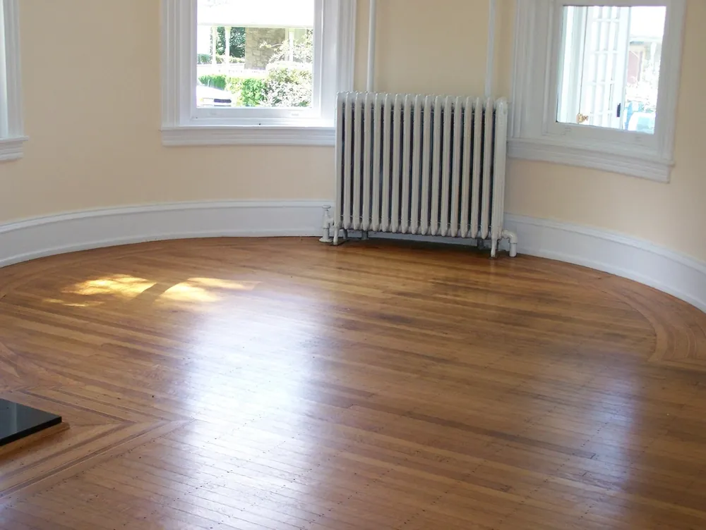 Sunlit empty room with a refinished hardwood floor and bay windows