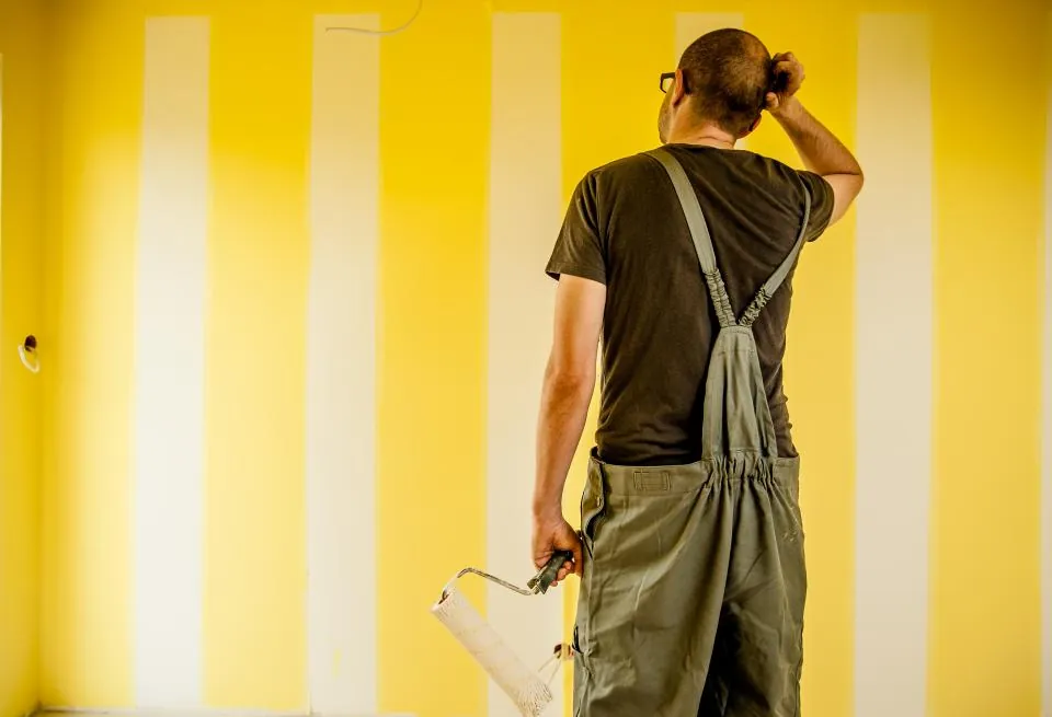 Painter standing in front of a yellow striped wall holding a paint roller