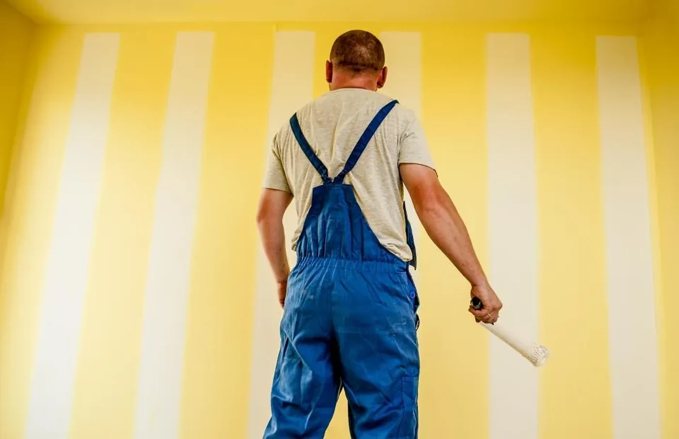 Painter in blue overalls facing a yellow striped wall